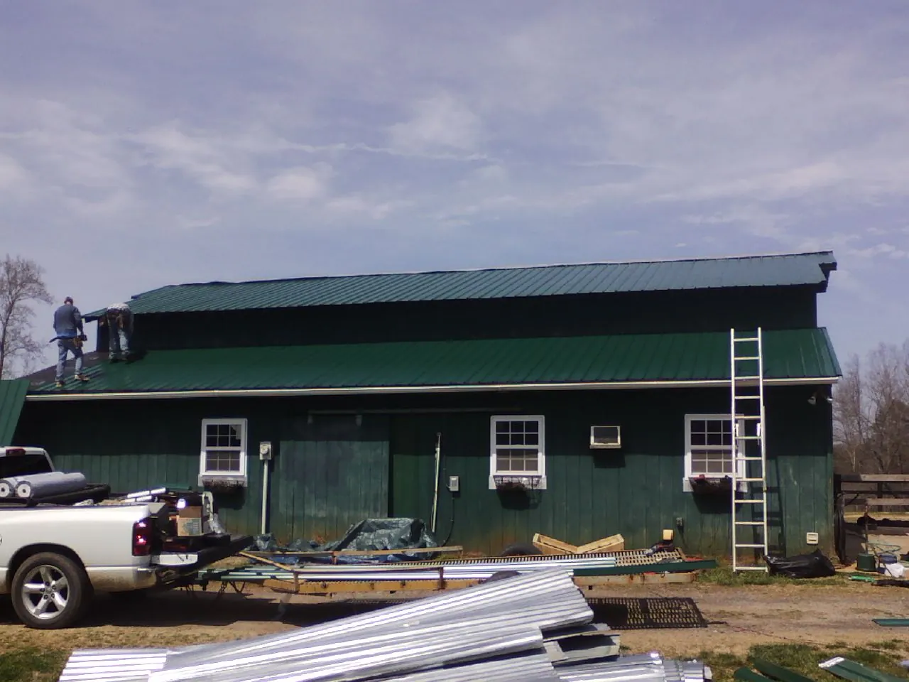 Crew installing green metal roofing on a large green barn in Farmington